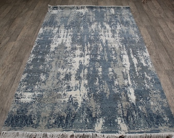 Puede incluir: Una alfombra rectangular con un patrón abstracto en tonos azul marino, gris pizarra y crema. El diseño consiste en motivos verticales, desgastados y texturizados que recuerdan a pinceladas por toda la superficie, rematada con flecos cortos de color blanco.