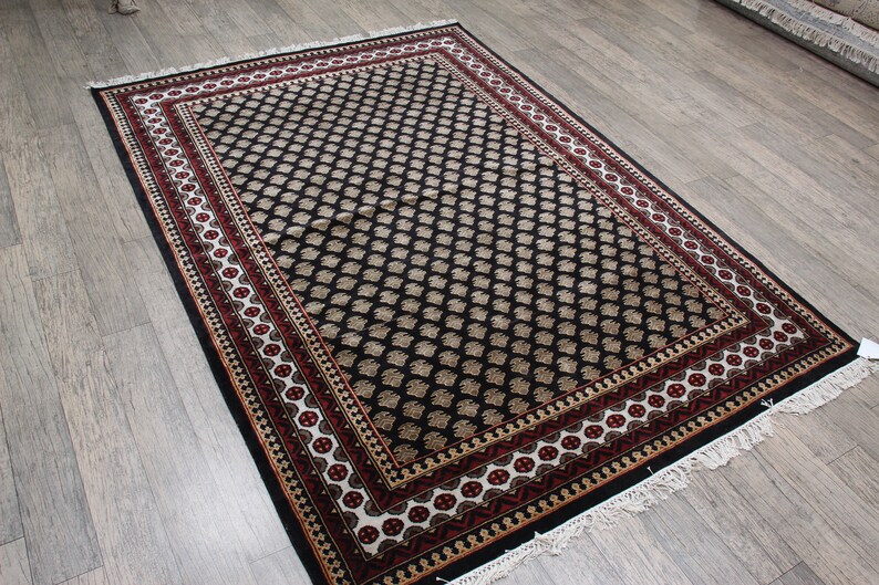 May include: A black and cream patterned rug with a red and white border. The rug has a fringe around the edges.