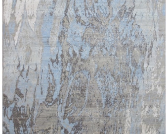 Puede incluir: Alfombra abstracta con tonos grises, azules y blancos. El diseño presenta un aspecto texturizado con patrones fluidos, creando una estética moderna y artística. La paleta de colores es neutra con toques de azul.