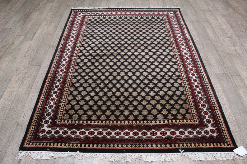 May include: Black and cream patterned rug with a red and white border. The rug has a traditional design with intricate details.