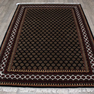 May include: Black and gold area rug with a detailed floral pattern and a multi-colored border. The rug has a white fringe.