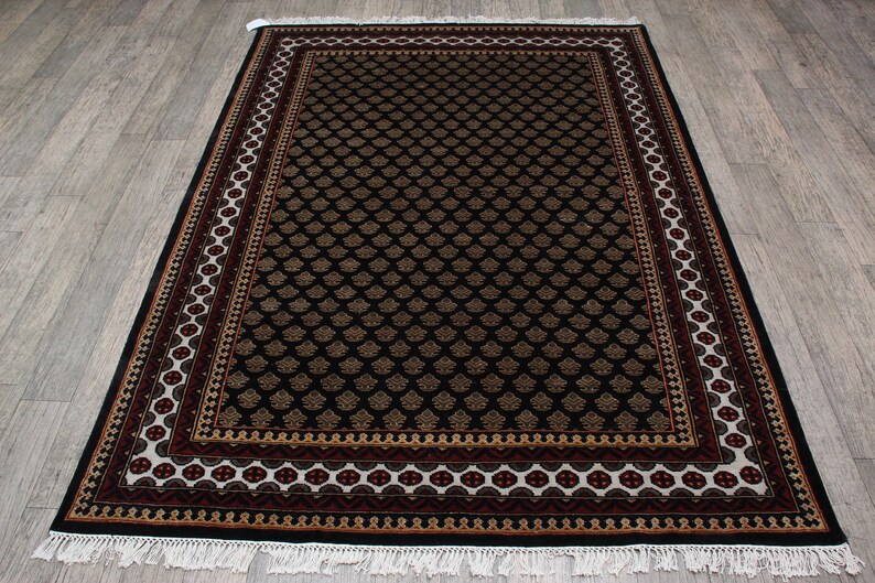 May include: Black and gold area rug with a detailed floral pattern and a multi-colored border. The rug has a white fringe.