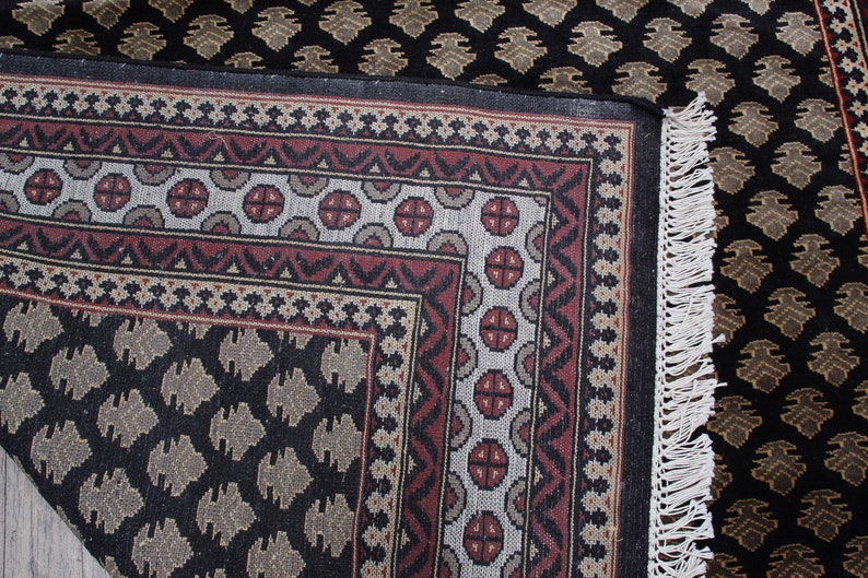 May include: A black and brown patterned rug with a white fringe. The rug has a geometric design with a central square surrounded by a border.
