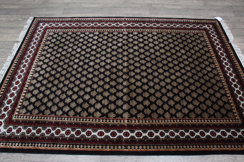 May include: Black area rug with a geometric pattern in beige and white. The rug has a red, white, and beige border.