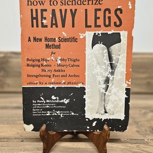 May include: Vintage book cover titled "How to Slenderize Heavy Legs" on a wooden stand. The cover is orange with black text and a black and white illustration of legs. The book addresses issues like bulging hips and heavy calves.