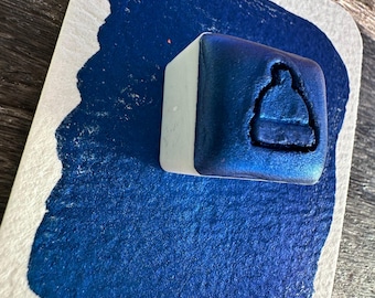 Puede incluir: Una almohadilla de tinta azul con un diseño en relieve de un gorro de invierno. La almohadilla de tinta está sobre una superficie blanca.