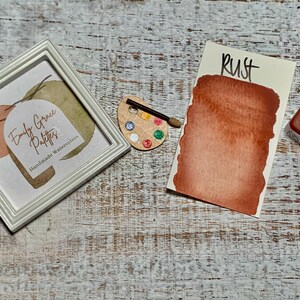 K&ouml;nnte beinhalten: Eine Aquarell-Farbpalette mit der Aufschrift "Rust" und einem braunen Aquarell-Farbmuster. Die Farbpalette befindet sich neben einem wei&szlig;en Rahmen mit dem Text "Emily Grace Patters Handmade Watercolors".