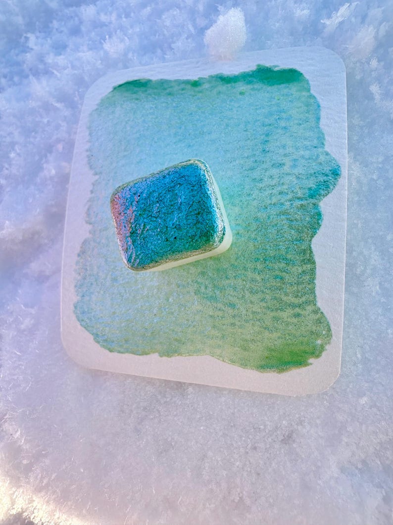 May include: A teal green and iridescent soap bar on a white and green watercolor paper background.