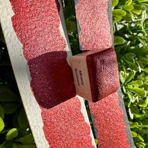 Puede incluir: Dos muestras de pintura roja con purpurina con un pequeño recipiente de pintura roja con purpurina etiquetado como "Misery Business".