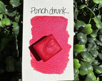 May include: A red watercolour paint pan with the text "Punch drunk" written on a white card.