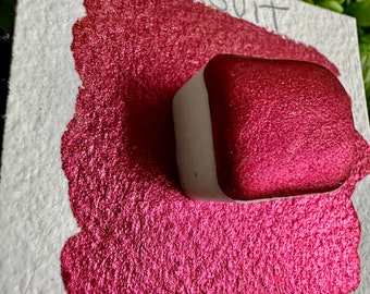 Puede incluir: Una pequeña bandeja cuadrada de pintura roja metálica con una etiqueta blanca que dice "Santa's Suit" sobre una superficie blanca.