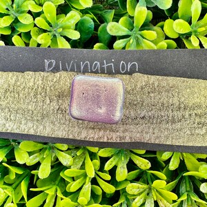 May include: A small, iridescent purple square with the word "Divination" written in white on a black background.