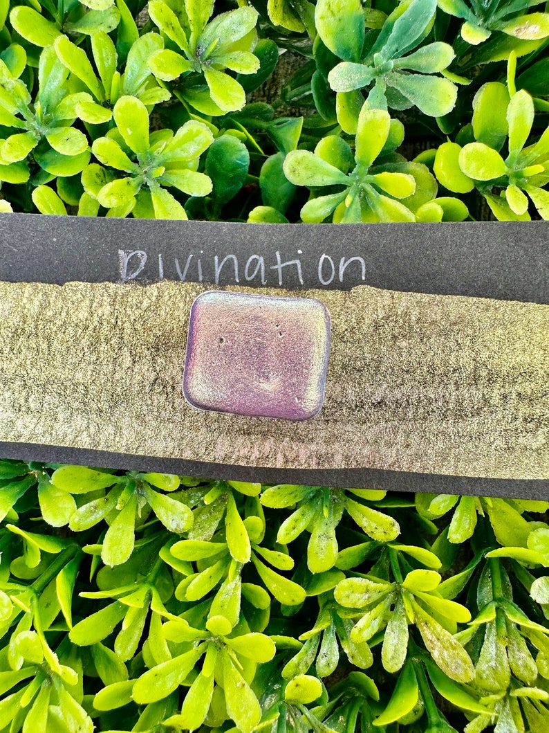 May include: A small, iridescent purple square with the word "Divination" written in white on a black background.