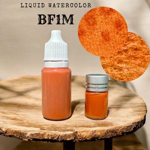 May include: Two bottles of orange liquid watercolor paint. The larger bottle has a white cap and the smaller bottle has a silver cap. The text "LIQUID WATERCOLOR BF1M" is visible in the image.