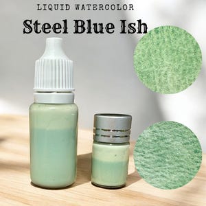 May include: Two bottles of liquid watercolor paint, one in a clear bottle with a white cap and the other in a silver bottle with a silver cap. The paint is a light green color with a hint of blue. The text "LIQUID WATERCOLOR" and "Steel Blue Ish" is visible in the image.