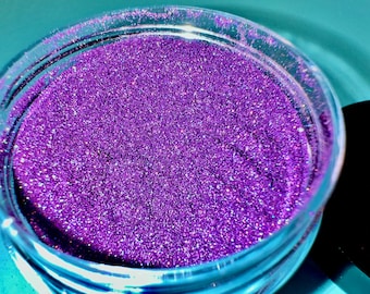 May include: A close-up of a jar filled with purple glitter. The glitter is very fine and has a slight iridescent sheen.