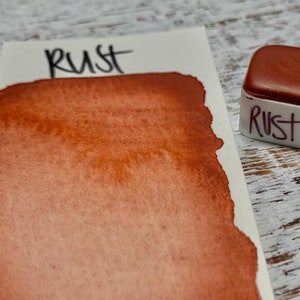 K&ouml;nnte beinhalten: Ein kleiner, quadratischer Beh&auml;lter mit rostfarbener Aquarellfarbe. Der Beh&auml;lter ist mit "Rust" beschriftet.