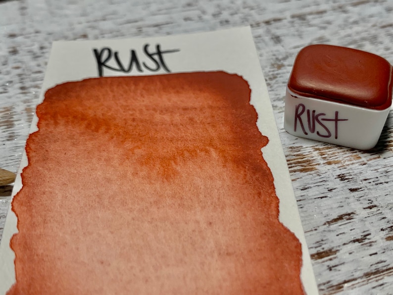 K&ouml;nnte beinhalten: Ein kleiner, quadratischer Beh&auml;lter mit rostfarbener Aquarellfarbe. Der Beh&auml;lter ist mit "Rust" beschriftet.
