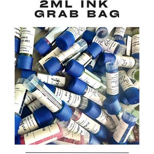 Puede incluir: Una colección de pequeños frascos de tinta con tapas azules y etiquetas blancas. El texto "2ML INK GRAB BAG" está en la parte superior de la imagen, con "EMILY GRACE PALETTES" en la parte inferior. Los frascos están llenos de varios colores.