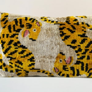 Puede incluir: Una almohada decorativa con fondo blanco y estampado de tigre amarillo y negro. La almohada est&aacute; hecha de una tela suave y mullida.