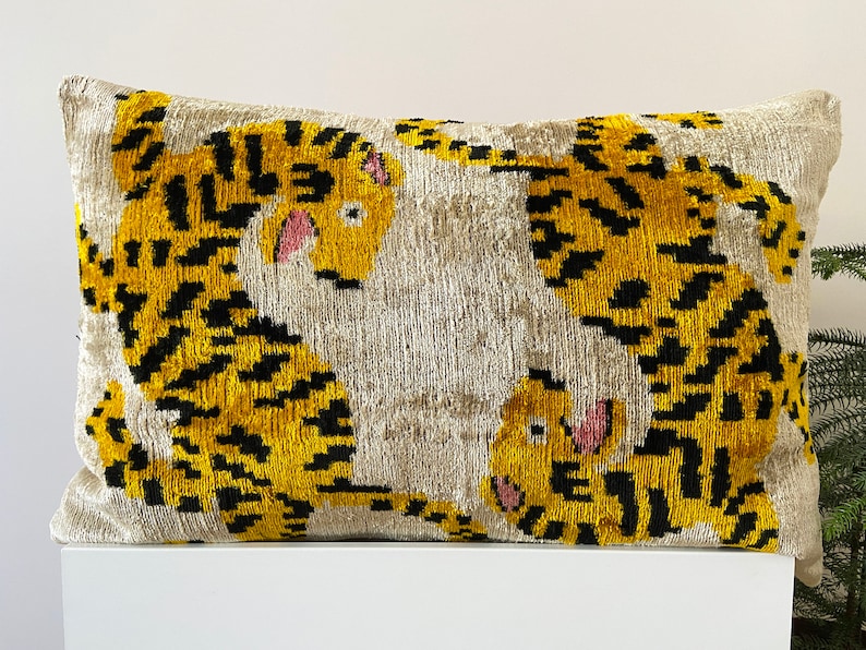 Puede incluir: Una almohada decorativa con fondo blanco y estampado de tigre amarillo y negro. La almohada est&aacute; hecha de una tela suave y mullida.