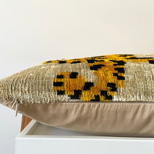 Puede incluir: Una almohada beige con cierre de cremallera. La almohada presenta un patr&oacute;n geom&eacute;trico en negro, amarillo y blanco.