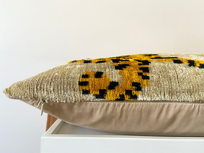 Puede incluir: Una almohada beige con cierre de cremallera. La almohada presenta un patr&oacute;n geom&eacute;trico en negro, amarillo y blanco.