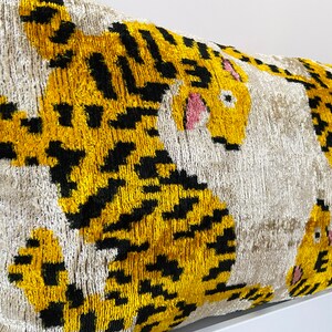 Puede incluir: Una almohada decorativa con fondo blanco y dos dise&ntilde;os de tigres amarillos y negros. Los tigres tienen la nariz y los ojos rosas.