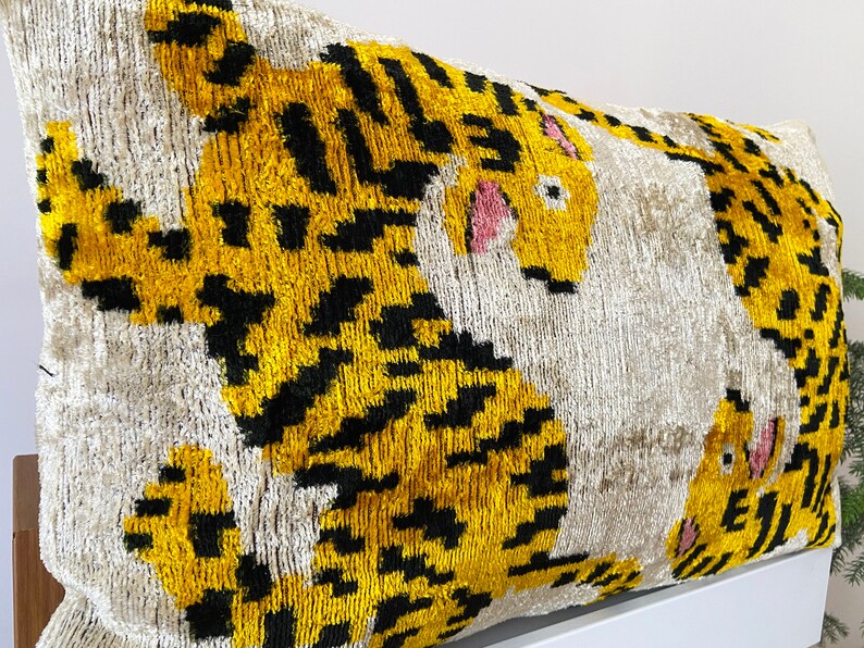 Puede incluir: Una almohada decorativa con fondo blanco y dos dise&ntilde;os de tigres amarillos y negros. Los tigres tienen la nariz y los ojos rosas.