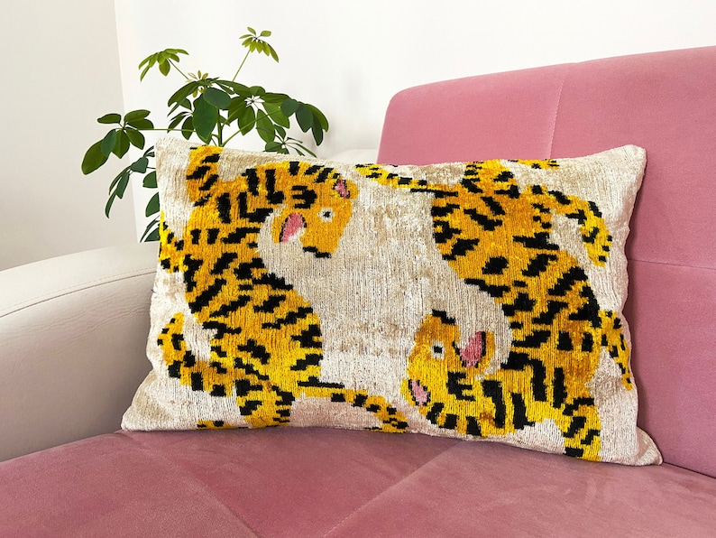Puede incluir: Una almohada decorativa con fondo blanco y dos dise&ntilde;os de tigres amarillos y negros. Los tigres se miran y tienen la nariz rosa.
