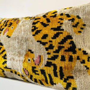 Puede incluir: Una almohada decorativa con fondo beige y estampado de tigre amarillo y negro.