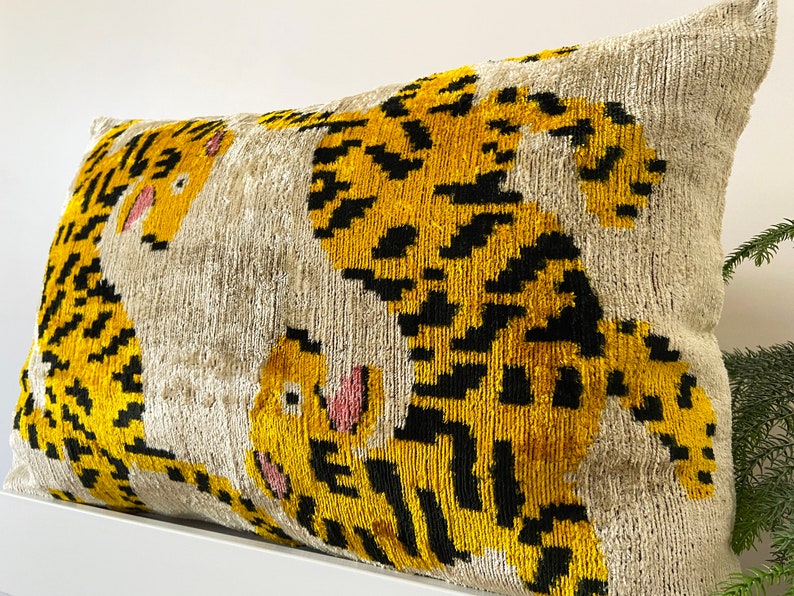 Puede incluir: Una almohada decorativa con fondo beige y estampado de tigre amarillo y negro.