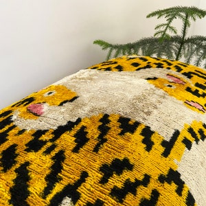 Puede incluir: Un coj&iacute;n de tiro amarillo y negro con un dise&ntilde;o de tigre sobre un fondo blanco. El coj&iacute;n est&aacute; hecho de una tela suave y mullida.