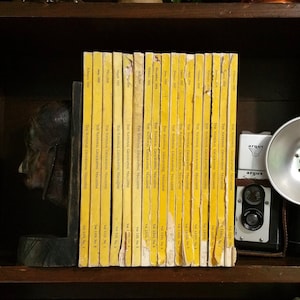 Op de afbeelding: Een boekenkast gevuld met vintage exemplaren van The National Geographic Magazine, daterend uit het begin van de 1900s. De ruggen zijn geel met zwarte tekst en de tijdschriften zijn chronologisch gerangschikt.