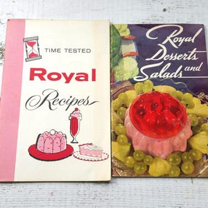 May include: Two vintage cookbooks with a white background and red and black text. The cookbook on the left is titled "Royal Recipes" and features an hourglass with the text "Time Tested". The cookbook on the right is titled "Royal Desserts and Salads" and features a pink gelatin mold with red cherries on top.
