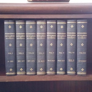 May include: A collection of eight matching dark blue hardcover books titled "International Encyclopedia of Reference." Each volume is labeled with a Roman numeral and a section of the alphabet. Gold decorative accents are visible on the spines.