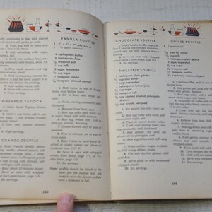 May include: An open vintage cookbook page featuring recipes for Vanilla Souffle, Pineapple Tapioca, Orange Souffle, Chocolate Souffle, and Coffee Souffle. The text is printed in black ink on off-white paper with small red and black illustrations.
