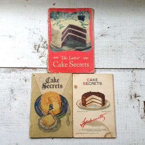 May include: Three vintage cookbooks with red and yellow covers featuring images of cakes and the text "Cake Secrets".