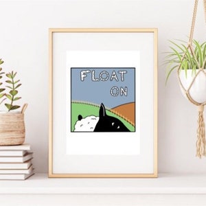 May include: A framed print featuring a black and white illustration of a sheep and a dog on a hill. The text "FLOAT ON" is displayed in a blue box above the animals.