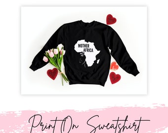 May include: A black long-sleeve sweatshirt featuring a white graphic of the African continent with the text "MOTHER AFRICA" and a stylized facial profile. The design is centered on the chest, and the garment has a crew neckline and ribbed cuffs.
