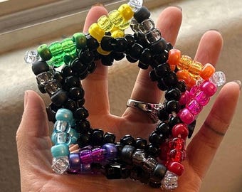 May include: A rainbow coloured star-shaped kandi bracelet made with black and clear beads.