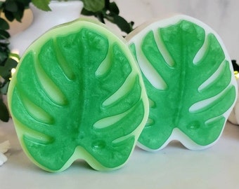 May include: Two green and white monstera leaf shaped soap bars. The soap bars are made with a translucent green and white color and have a shiny finish.