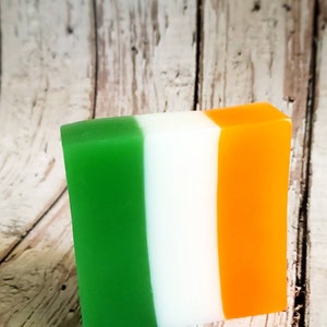 May include: A bar of soap with green, white and orange stripes. The soap is shaped like a rectangle and is sitting on a wooden surface.