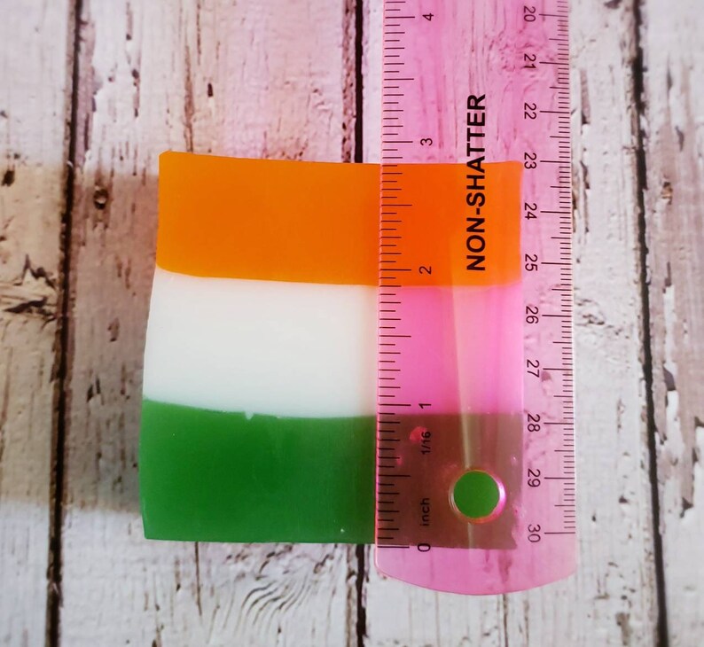 May include: A rectangular bar of soap with three layers of colour: orange, white, and green. The soap is measured against a ruler, showing it is approximately 7 cm long.