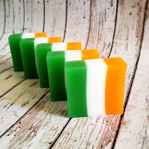 May include: Five bars of soap arranged in a row. The bars are layered in green, white, and orange, resembling the Irish flag.