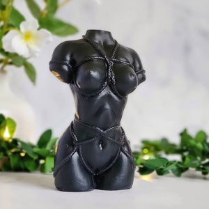 May include: Black resin sculpture of a female torso with rope tied around the body. The sculpture is a modern art piece.