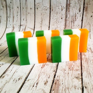 May include: Six bars of soap with green, white and orange stripes. The soap bars are arranged in a row on a wooden surface.