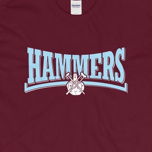 May include: A maroon t-shirt with a light blue arch design that says "HAMMERS" with a crossed hammer graphic inside the arch.