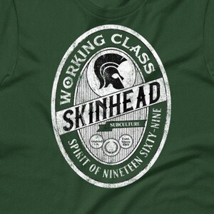 Puede incluir: Camiseta verde con un logotipo blanco de estilo vintage que dice "Working Class Skinhead Spirit of Nineteen Sixty-Nine". El logotipo presenta un casco espartano.