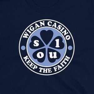 May include: Navy blue t-shirt with a white circle logo that says "Wigan Casino Keep The Faith" and features a blue four-leaf clover with the letters "S.O.U.L" inside.